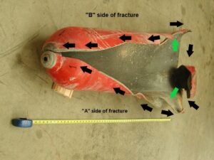 View of the ruptured cylinder in the as-received condition. A primarily axial rupture split the cylinder wide open. The axial fracture turned circumferential in opposing directions at the base of the cylinder. The two fracture halves are labeled “A” and “B” for examination identification purposes. The green arrows indicate the rupture initiation site. The smaller black arrows indicate the direction of fracture propagation.
