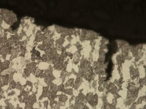 High magnification photomicrograph of the unetched cross-section along the fracture surface reveals axial corrosion penetrations, indicating active corrosion along the pre-existing crack. 