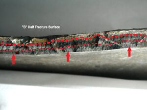 The “B” side axial fracture surface after cleaning reveals black oxide covered pre-existing crack patterns along the cylinder ID surface, extending across approximately 80% of the cylinder wall. A slight variation in the black deposit suggests a two-stage pre-crack (between dashed lines).