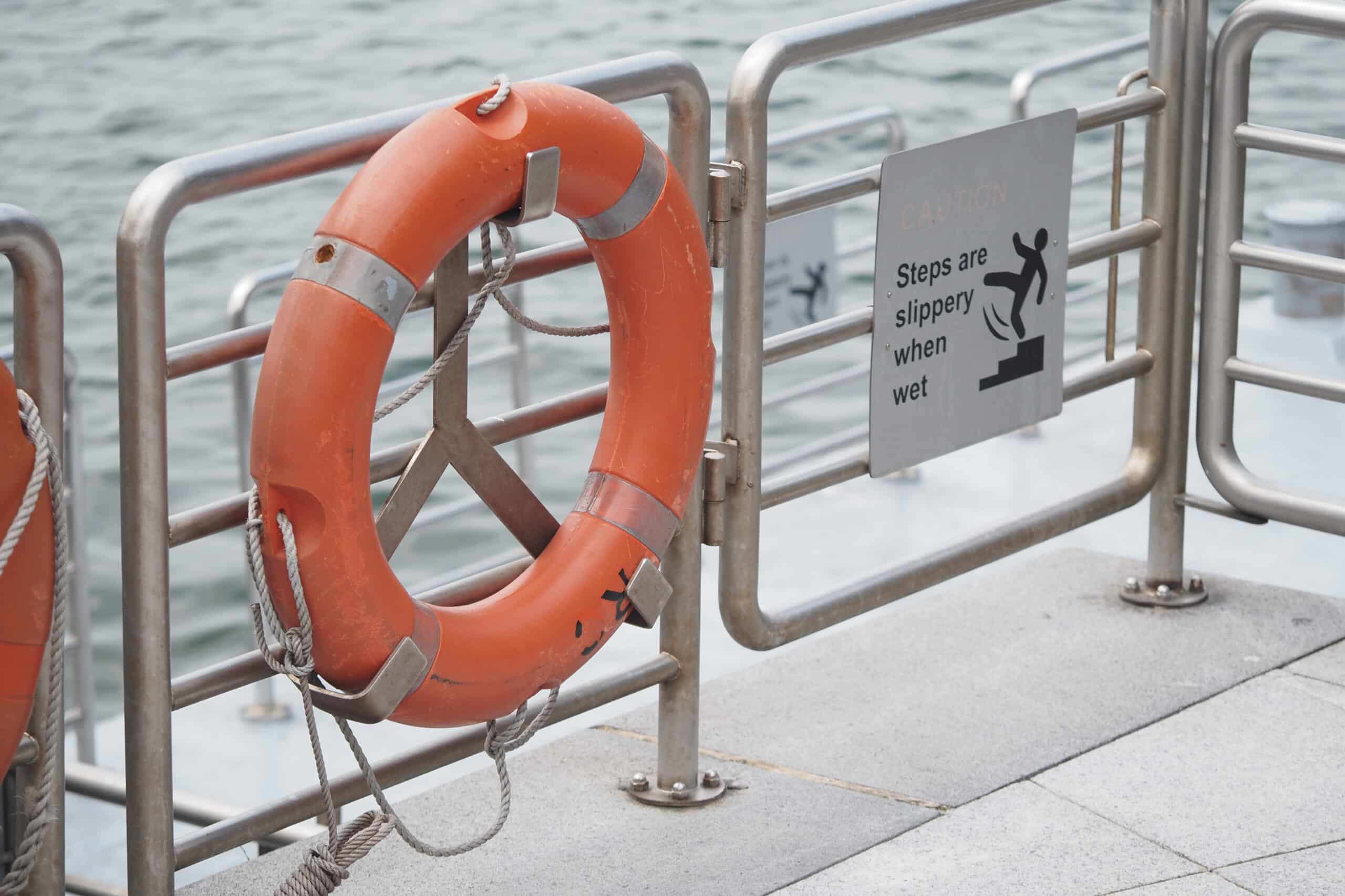 A life ring hangs on a railing next to a wet steps warning sign. 