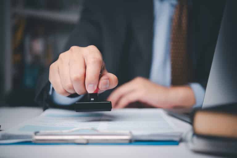 Businessman stamping contract document on desk, symbolizing legal approval, corporate agreement, and business authorization process. Expert Human Factors Consulting