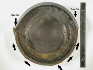 A view of the circumferential fracture at the cylinder bottom revealed after sectioning. The bottom internal surface displays some corrosion (brown staining). The fracture propagation direction is indicated by the arrows. 