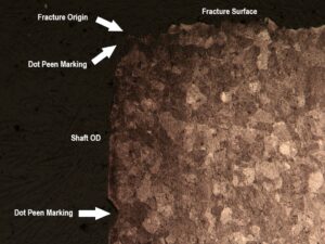 An optical microscopic image of a longitudinal cross-section through the fracture origin shows an impression in the surface at the fracture origin, which is the result of dot peen marking. An additional impression is observed below the fracture origin.