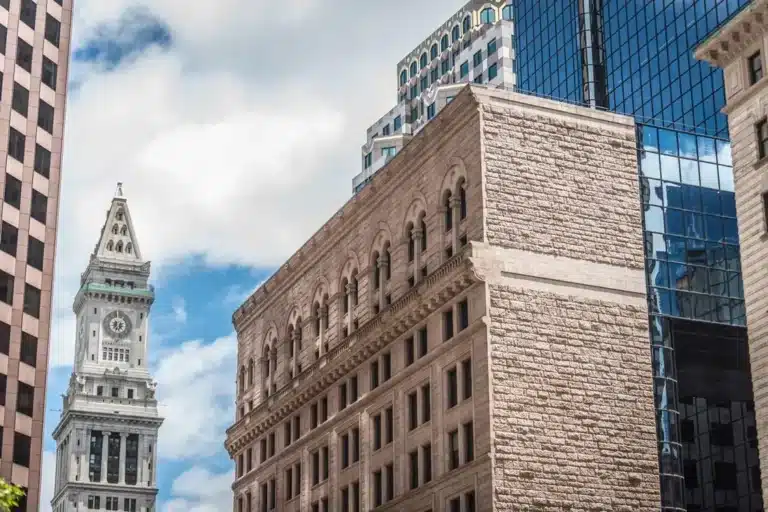 This image shows the historic Boston Custom House Tower (left clock tower) rising behind downtown stone and glass commercial architecture in Boston, Massachusetts