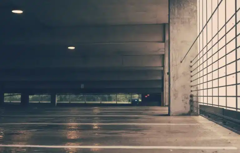 The image shows an empty, indoor concrete parking garage with a wet or reflective floor and industrial lighting.