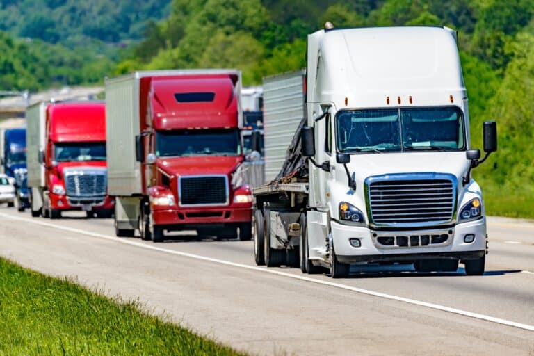 Une ligne continue de camions à dix-huit roues roule sur une autoroute inter-États dans le Tennessee. Les vagues de chaleur qui s'élèvent de la chaussée donnent un bel effet de miroitement aux véhicules et aux arbres situés derrière le camion de tête. Sécurité et conformité des camions